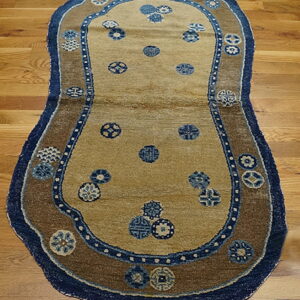 Tan rug with dark blue trim and brown border featuring scattered blue medallions on wood flooring.