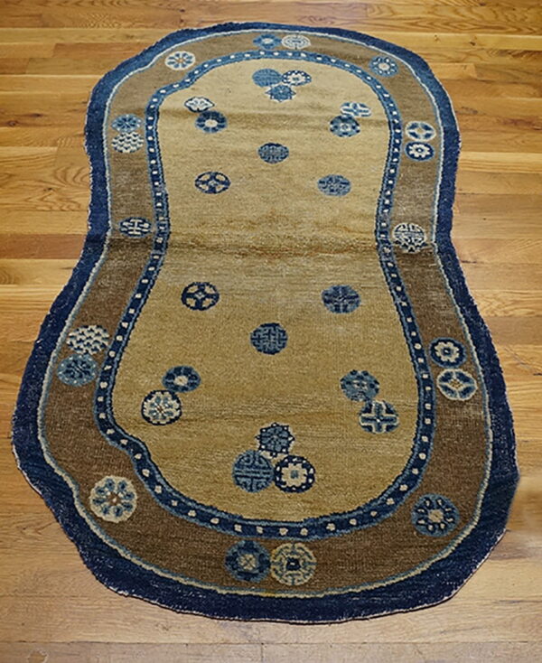 Tan rug with dark blue trim and brown border featuring scattered blue medallions on wood flooring.
