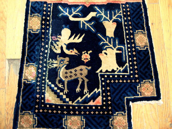 Dark blue rug with tan figures of deer and animals, detailed borders, resting on light wood floors.