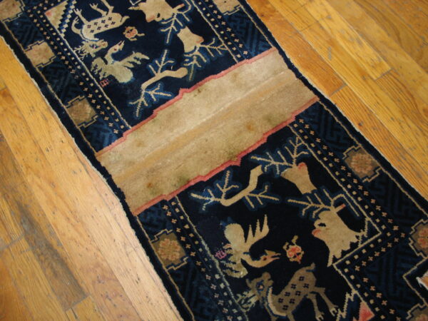 A low-pile runner with navy blue and beige stylized animal patterns lies diagonally on distressed hardwood.
