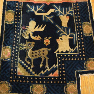 Dark blue high-pile rug with beige deer pattern and geometric borders resting on light hardwood flooring.