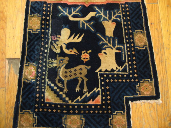 Dark blue high-pile rug with beige deer pattern and geometric borders resting on light hardwood flooring.