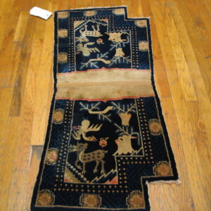 Deep navy blue rug with beige animal scenes and pink accents rests on wide plank wood flooring.