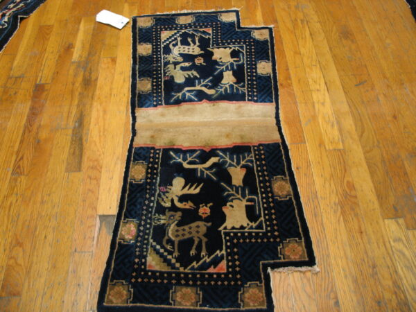Deep navy blue rug with beige animal scenes and pink accents rests on wide plank wood flooring.