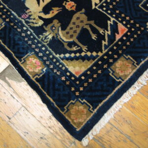 Dark blue rug with tan animal and geometric patterns and white fringe lies on rustic wood floor.