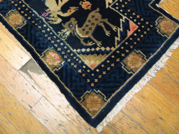 Dark blue rug with tan animal and geometric patterns and white fringe lies on rustic wood floor.