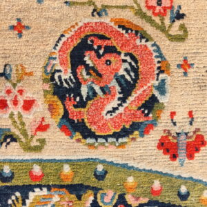 Close-up of a low-pile, multicolored rug showing a coral dragon and flowers on a cream background.