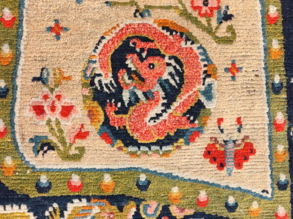 Close-up of a low-pile, multicolored rug showing a coral dragon and flowers on a cream background.