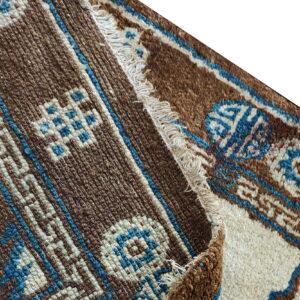 Geometric brown, cream, and blue rug textures meet at a folded edge with visible fringe.