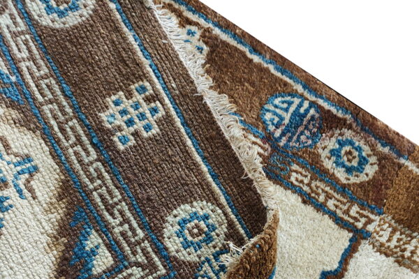 Geometric brown, cream, and blue rug textures meet at a folded edge with visible fringe.