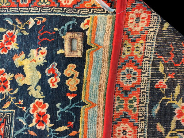 Woven rug detail features navy background, red and yellow patterns, geometric borders, and a rolled-up red-bound edge.