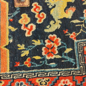 Close-up of a dark blue patterned rug featuring a yellow dragon, red flowers, and an attached leather tag.