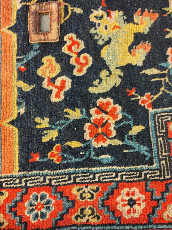 Close-up of a dark blue patterned rug featuring a yellow dragon, red flowers, and an attached leather tag.