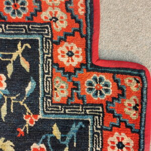 Detail of a rug featuring navy, coral, and teal floral patterns framed by a geometric border on gravel.