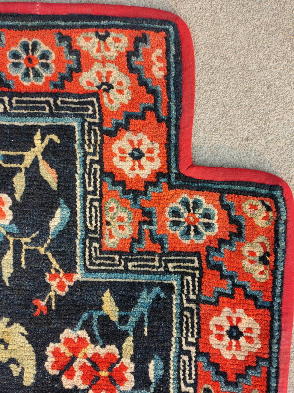 Detail of a rug featuring navy, coral, and teal floral patterns framed by a geometric border on gravel.