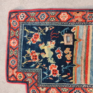 Brightly colored rug with blue field, red border, and striped pattern resting on a textured gray floor.