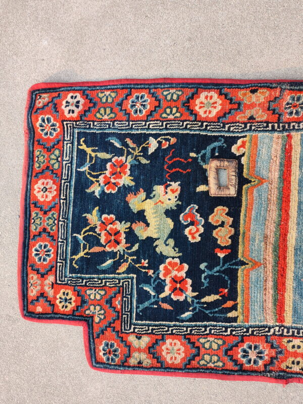 Brightly colored rug with blue field, red border, and striped pattern resting on a textured gray floor.