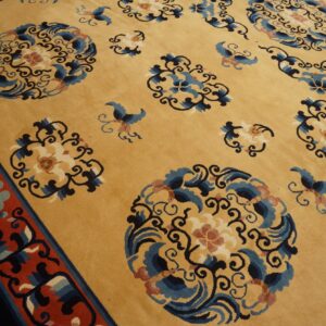 Close view of a gold rug with scattered blue, navy, and rust floral motifs and a thick red border.