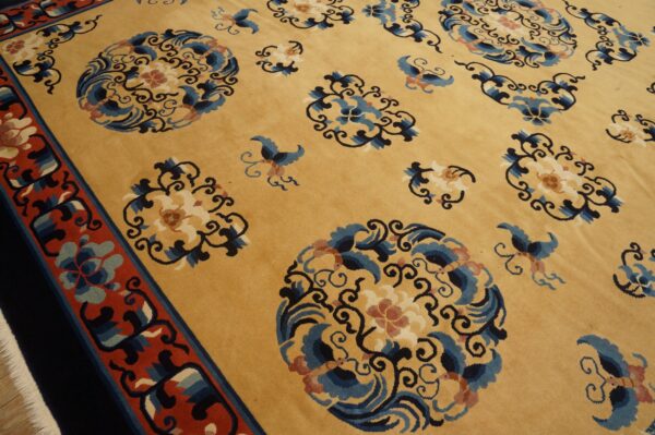 Close view of a gold rug with scattered blue, navy, and rust floral motifs and a thick red border.