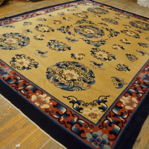 Golden yellow rug with blue medallions and a broad terracotta and navy floral border on wood planks.