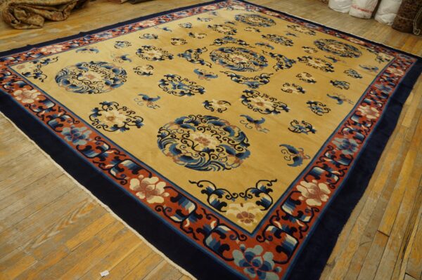 Golden yellow rug with blue medallions and a broad terracotta and navy floral border on wood planks.
