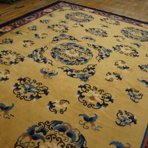 Golden yellow rug with scattered blue floral motifs and a coral border, laid on wooden floorboards.