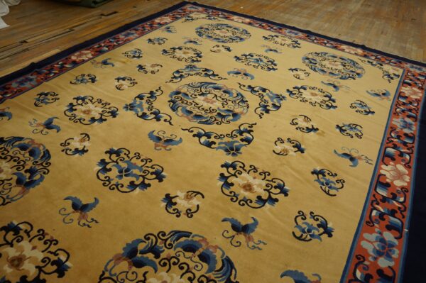 Golden yellow rug with scattered blue floral motifs and a coral border, laid on wooden floorboards.