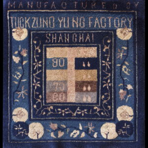 Close-up of a blue rug with tan floral motifs framing factory text and a numbered color block design.