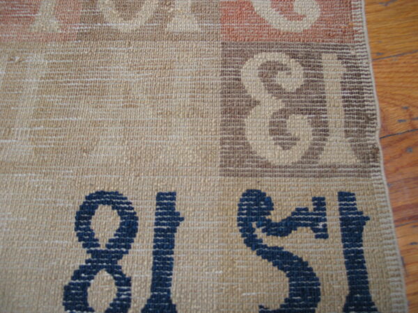 Flatweave rug detail showing beige, rust, brown, and navy numerical patterns next to a wood floor.