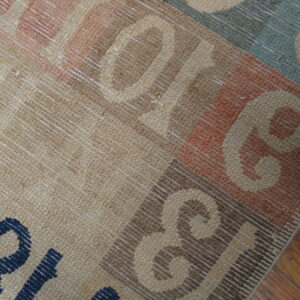 Close-up shows a multicolored flatweave rug with large graphic letters on brown wooden plank flooring.