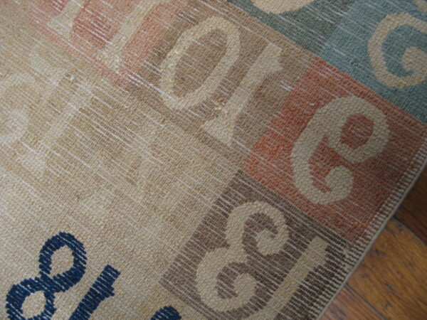 Close-up shows a multicolored flatweave rug with large graphic letters on brown wooden plank flooring.