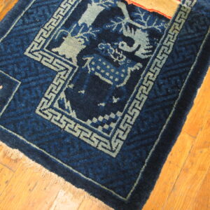 Dark blue rug featuring light blue fretwork borders and figurative designs on golden hardwood floors.