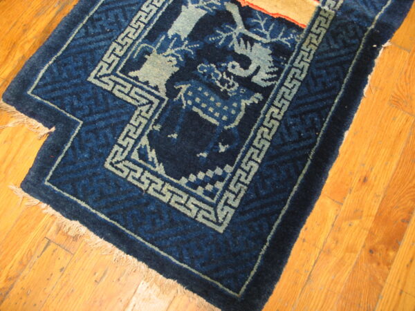 Dark blue rug featuring light blue fretwork borders and figurative designs on golden hardwood floors.
