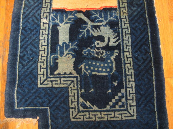 Close-up of a navy and pale blue rug showing stylized deer and tree motifs with a geometric greek key border on wood flooring.