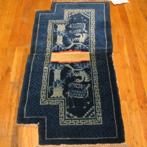 A stepped blue rug with creature patterns and a tan repair patch lies on orange hardwood flooring.