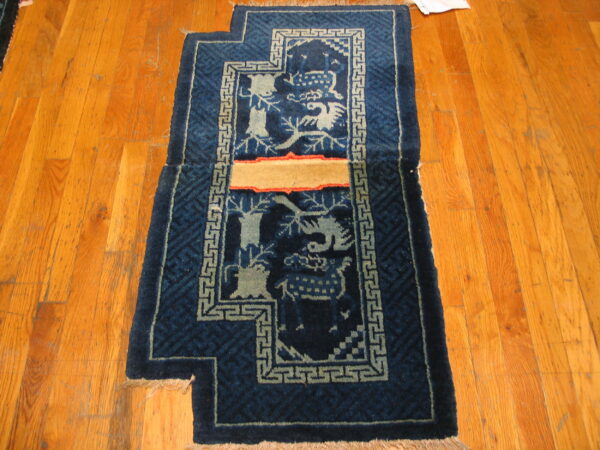 A stepped blue rug with creature patterns and a tan repair patch lies on orange hardwood flooring.