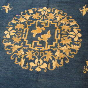 Detailed view of a deep blue rug featuring tan floral, butterfly, and stepped geometric motifs.