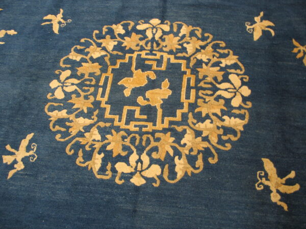 Detailed view of a deep blue rug featuring tan floral, butterfly, and stepped geometric motifs.