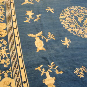 Blue rug featuring scattered light tan floral and vase motifs bordered by a geometric fret pattern.