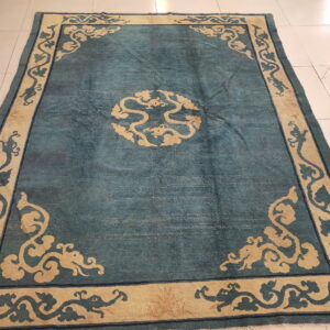 Teal patterned rug featuring a large beige border with dragon and cloud scroll designs on white tiled flooring.