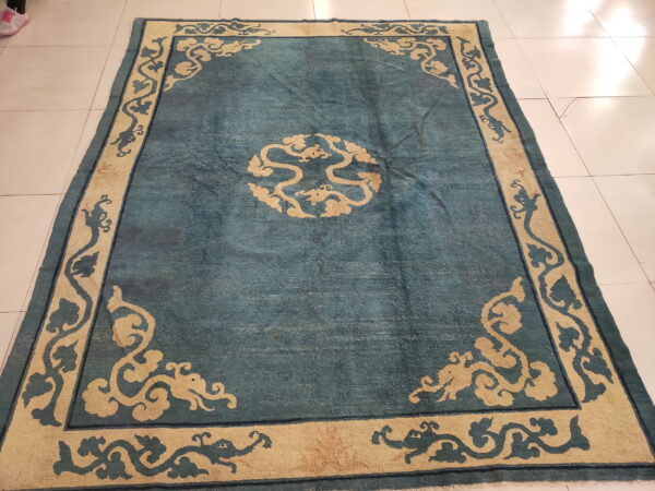 Teal patterned rug featuring a large beige border with dragon and cloud scroll designs on white tiled flooring.