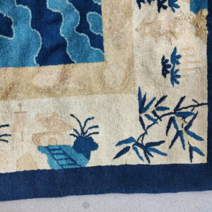 A thick-piled rug corner in blue and beige featuring stylized clouds, bamboo, and a navy border.