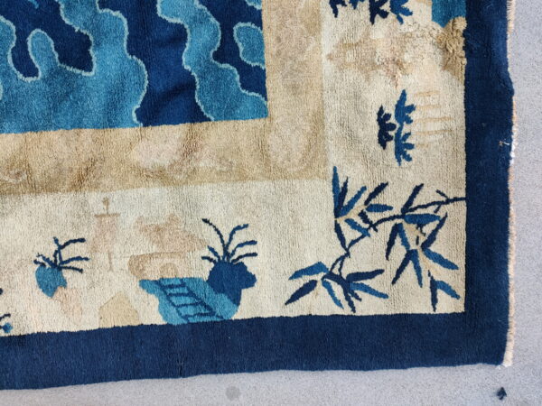 A thick-piled rug corner in blue and beige featuring stylized clouds, bamboo, and a navy border.