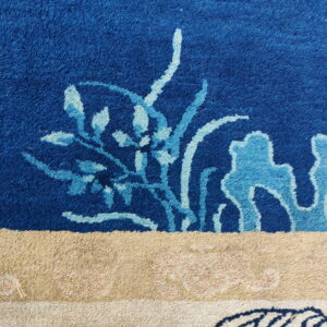 Plush rug detail features deep blue pile with light blue floral motifs above a thick beige and cream border.