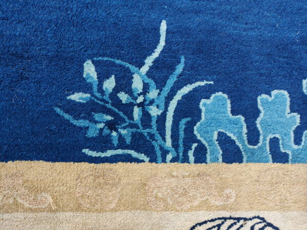 Plush rug detail features deep blue pile with light blue floral motifs above a thick beige and cream border.