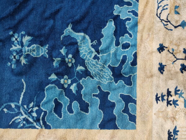 High-pile rug detail showing a stylized bird and flowers in indigo and light blue, framed by a cream border.