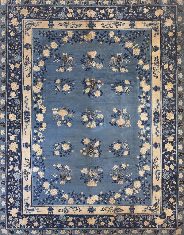Ornate blue rug with beige and navy floral patterns and repeating vessel and bird motifs in the field.