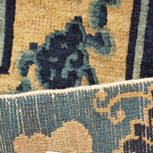 Close-up of a blue and tan patterned rug showing the plush pile face and woven reverse edge.