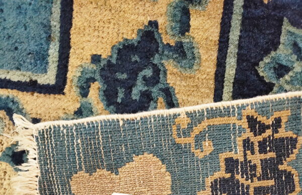Close-up of a blue and tan patterned rug showing the plush pile face and woven reverse edge.