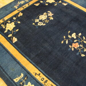 A plush dark navy rug with cream, pink, and blue floral motifs and a golden ochre border on wood floor.